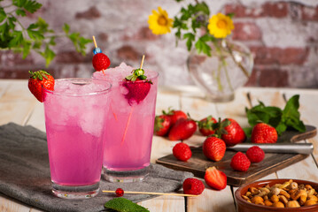 Glasses of ice with strawberry and raspberry soda made from fruit juice, next to a cutting board with pieces of fruit. Close-up.