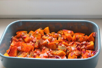 Sheet pan with pieces of butternut squash, onion, herbs and spices. Preparing pumpkin for a roast. Selective focus.