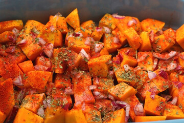 Sheet pan with pieces of butternut squash, onion, herbs and spices. Preparing pumpkin for a roast. Selective focus.