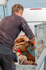 Construction worker unloading a trailer with wooden garbage in a recycling station 