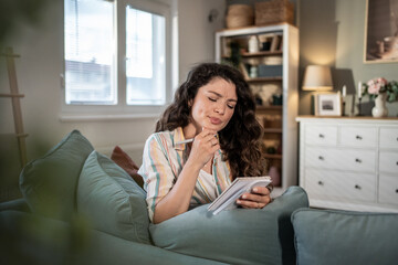 Obraz premium Thoughtful woman making notes in notebook at home