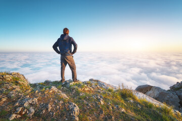 Man stands over the cover clouds on the edge of the abyss and looks on sun.