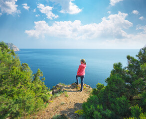 A girl with a standing on the cliff on the hill and watching the calm sea in the bay.