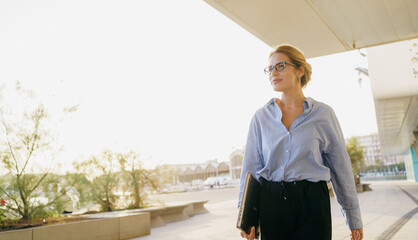 A confident businesswoman is walking outdoors in an urban city environment during the daytime