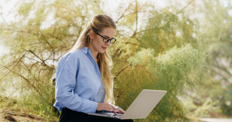 A businesswoman works on her laptop outdoors, balancing her career and personal life