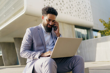 A professional man is utilizing a laptop while on the phone in a modern outdoor environment