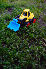A vibrant yellow toy bulldozer is positioned on a patch of green grass showcasing its working scoop as it appears to be digging The sunny day adds to the playful atmosphere