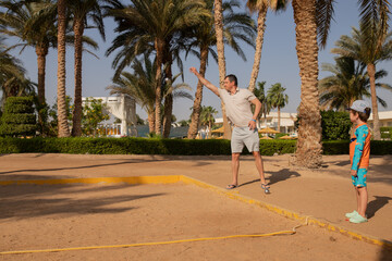 Man and boy playing petanque in hot country, father and son in hotel playing on sand