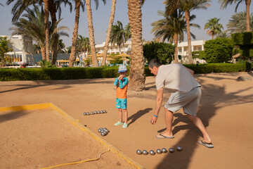 Man and boy playing petanque in hot country, father and son in hotel playing on sand