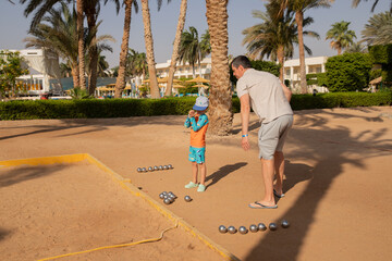 Man and boy playing petanque in hot country, father and son in hotel playing on sand