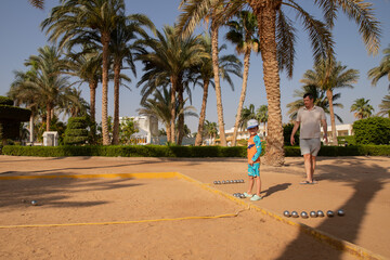 Man and boy playing petanque in hot country, father and son in hotel playing on sand