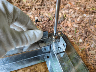 Close-up of a hand in a white glove assembling a metal frame. DIY outdoor project and handyman manual skills