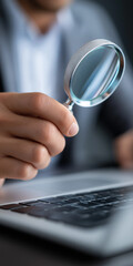 Fototapeta na wymiar A man is holding a magnifying glass over a laptop. Concept of curiosity and investigation, as if the man is trying to uncover something hidden or important on the laptop screen
