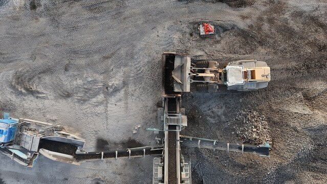 Aerial view of a loader feeding a screener with debris at a construction site. Industrial workflow in action, showing heavy machinery and material separation from above.

