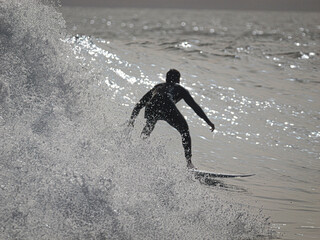 SILHOUETTE, CLOSE UP: Surfer in a wetsuit rides a glistening wave. Backlighting highlights splashing water droplets as he carves along the face of the wave. Amazing surf conditions at Canary Islands.