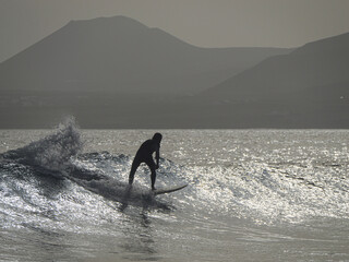 SILHOUETTE, CLOSE UP: Surfer generates speed as he rides along glowing empty wave with volcanic mountains silhouetted in the background. Stunning scenery and amazing surf conditions at Canary Islands.