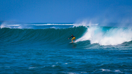 Experienced surfer in yellow shorts riding on a massive wave lifted by offshore wind. Clear blue Atlantic Ocean and powerful summer swell set the stage for amazing surfing conditions at Lanzarote.