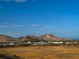 Island village with typical white buildings surrounded by dry volcanic landscape. Picturesque contrasts between whitewashed houses, bright blue skies and earth tones throughout the Canary Islands. © helivideo