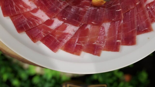 Gourmet iberian acorn fed ham rotating gracefully on pristine white ceramic plate, showcasing premium spanish charcuterie delicacy with elegant slow motion movement