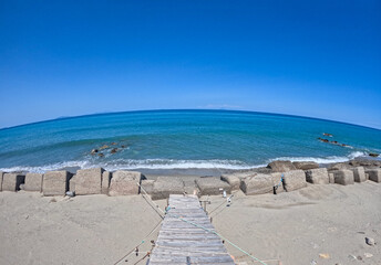 Panorama of the Mediterranean Sea seen with fish eye lens from the Sicilian coast with wooden staircase leading to the beach. The photo was taken in Messina on a sunny day