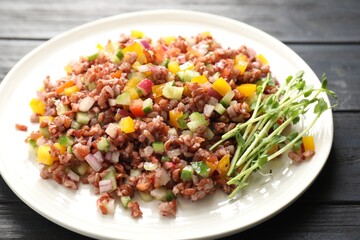 Tasty salad with brown rice on black wooden table, closeup