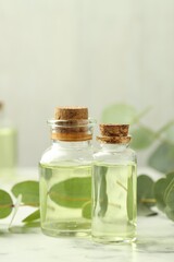 Bottles of essential oil and eucalyptus leaves on white marble table, closeup
