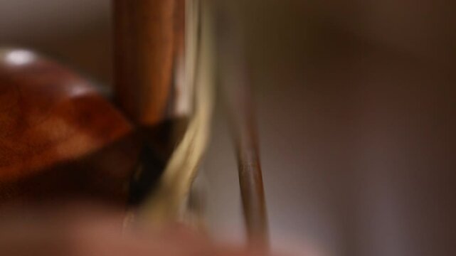 A close-up shot captures a musician's hands skillfully playing a traditional kamancheh, a spike fiddle, drawing the bow across its strings in a dynamic and focused musical performance.