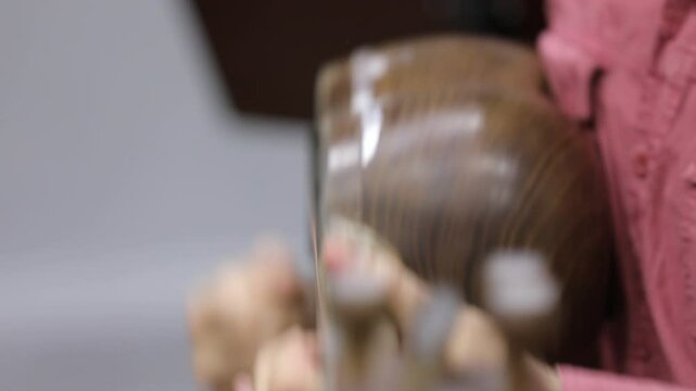 A close-up shot captures a musician's hands skillfully playing a traditional kamancheh, a spike fiddle, drawing the bow across its strings in a dynamic and focused musical performance.