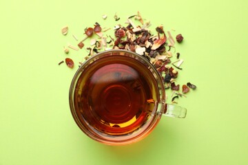 Delicious herbal tea in glass cup and dry leaves on light green background, flat lay