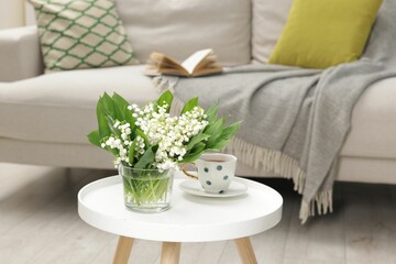 Bouquet of beautiful lily-of-the-valley and cup of tea on coffee table indoors