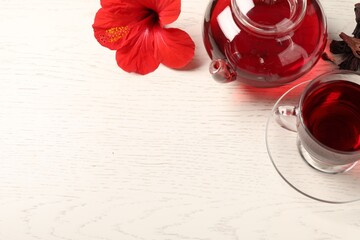 Delicious hibiscus tea in glass cup, teapot, dry roselle sepals and flower on light wooden table,...