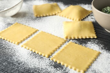 Uncooked ravioli, stuffing and flour on wooden table, closeup