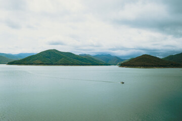 Mountain-ringed reservoir beneath looming rain clouds, capturing the calm before a storm in a...