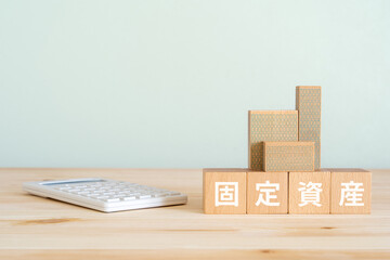 固定資産と書かれたブロック、不動産の模型、電卓