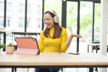 A woman is sitting at a table with a pink tablet and a cell phone. She is wearing headphones and...