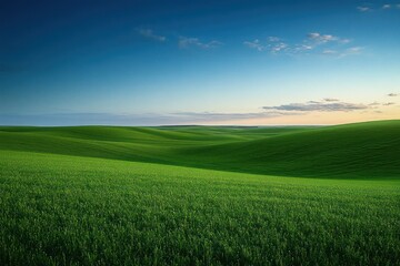 Obraz premium Rolling green hills under a clear blue sky with scattered clouds at sunset creating a peaceful and serene atmosphere