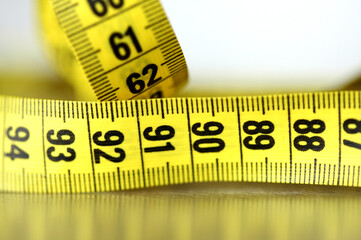 Close-up of a yellow measuring tape  on a white background, with reflection under.Perfect...