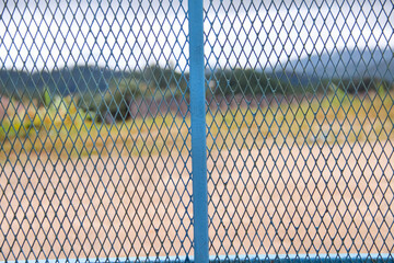 Blue mesh metal fence wall on mountain view background