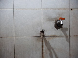 Two outdated water taps are mounted on a dirty white tile wall