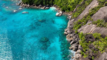 Fototapeta premium A rocky coastline with striking turquoise water and dense green vegetation on the slopes. Seychelles, Mahe.
