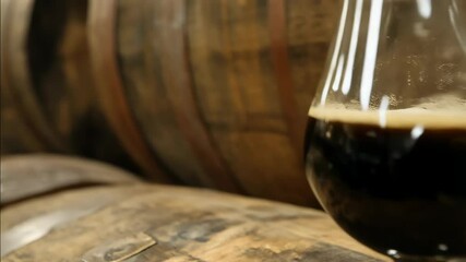 Craft dark ale in a tasting glass with barrel background for beer enthusiasts