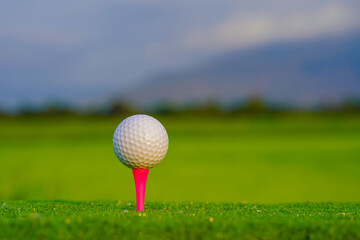 Close-up golf ball on tee with blur green bokeh background.