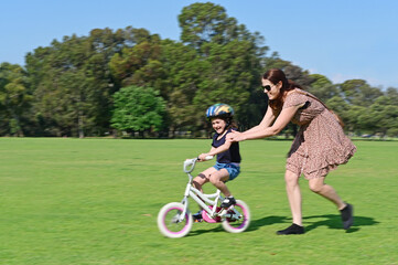 Mother teaching daughter to ride bike on park green grass motion blur