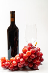 Fresh red grapes, an unopened bottle of wine, and an empty wineglass are arranged on a white background, ready for a tasting