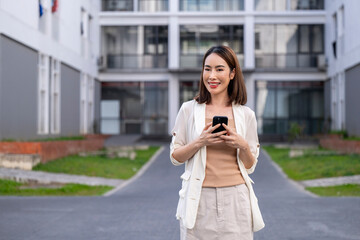 Fototapeta premium A woman is standing in front of a building with a cell phone in her hand