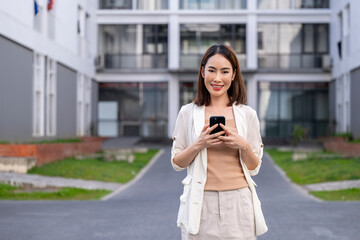 Fototapeta premium A woman is standing in front of a building with a cell phone in her hand
