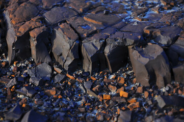 Jagged basalt formation with deep cracks and scattered orange rock fragments—ideal for geological...