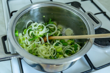leek simmering in pot on gas stove with wooden spoon