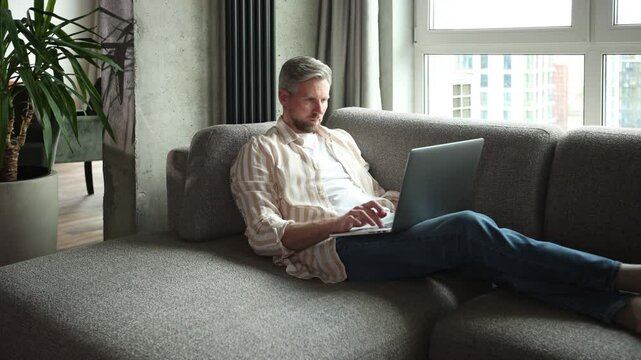 Happy young man sitting on sofa and working on laptop from home.