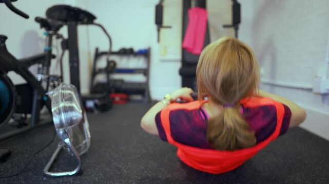 Senior woman sitting on the floor doing rowing exercises with a weight machine at home.